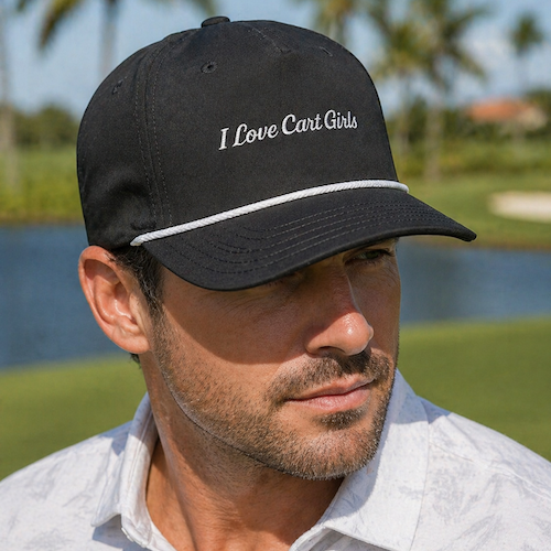 Man wearing a black cap that reads 'I Love Cart Girls' outdoors by a lake with palm trees in the background.