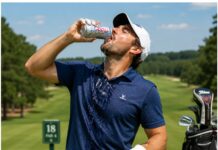 Golf Course Hydration Guide: What Your Beverage Says About Your Score Man in a navy polo and white cap drinks from a Coors Light can on a sunny golf course, with a golf bag nearby.