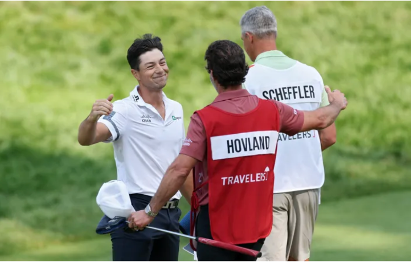 Three golfers on a green share a hug and smile; one wears a white shirt, another has 'HOVLAND' on a red bib, and a third has 'SCHEFFLER' on his back in white.