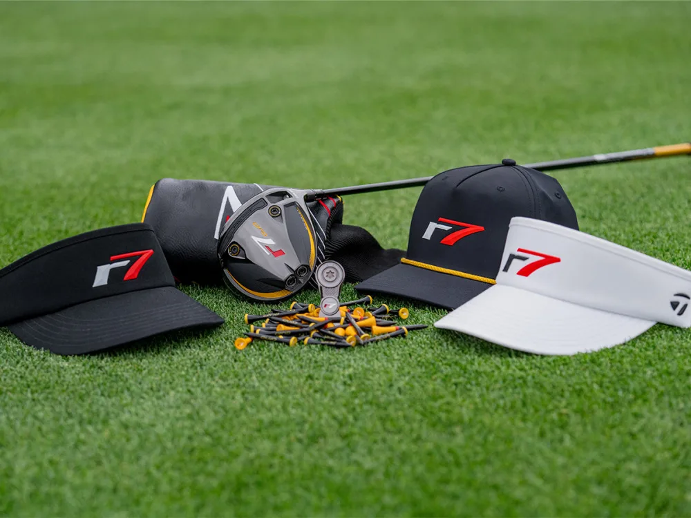F7-branded golf gear laid out on green grass: black and white visors, a golf club head, and scattered yellow tees