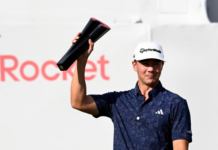 Winners, Losers & Payouts: Michael Thorbjornsen Breaks Through at the 2026 Rocket Classic, Outduels Xander Schauffele for First PGA TOUR Victory Golfer in a dark polo raises a black trophy above his head in celebration during a tournament. TaylorMade cap visible; partial 'Rocket' sign in background.