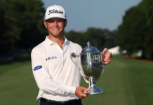 The Wyndham Championship Was More Than Just Another Tournament – Winners, Losers, and Payouts Male golfer in a white polo and Titleist cap smiles while holding a large silver trophy on a sunny golf course sunlit fairway.